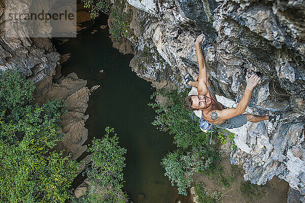 Mann klettert auf überhängendem Kalksteinfelsen in Laos