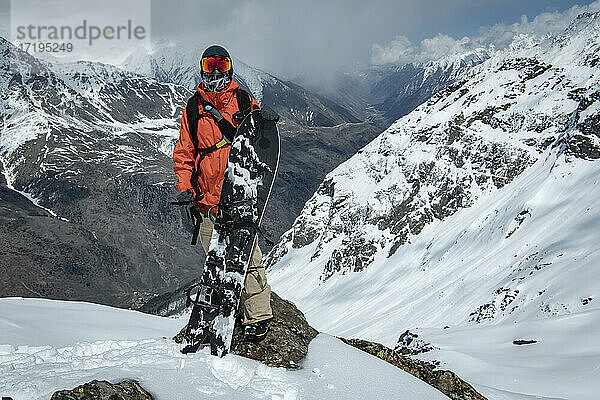 Mann mit Snowboard vor schneebedeckten Bergen im Urlaub