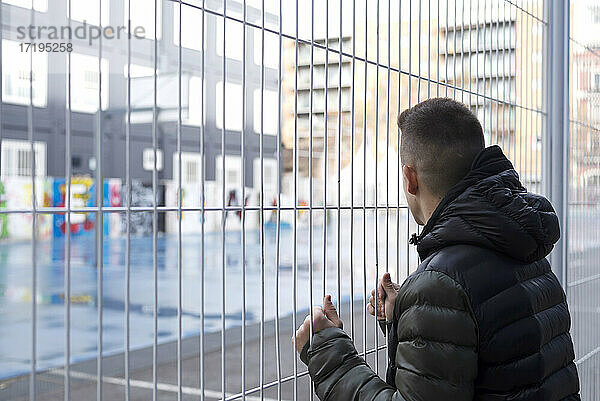 Rückansicht des Mannes  der am Zaun steht