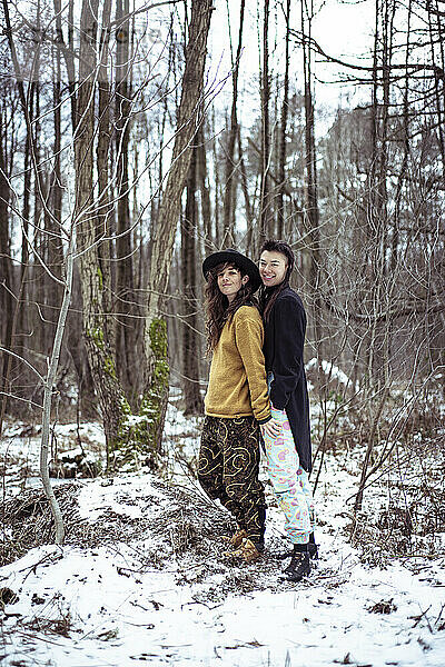 flippiges junges gemischtrassiges queeres Paar lächelt im verschneiten Wald