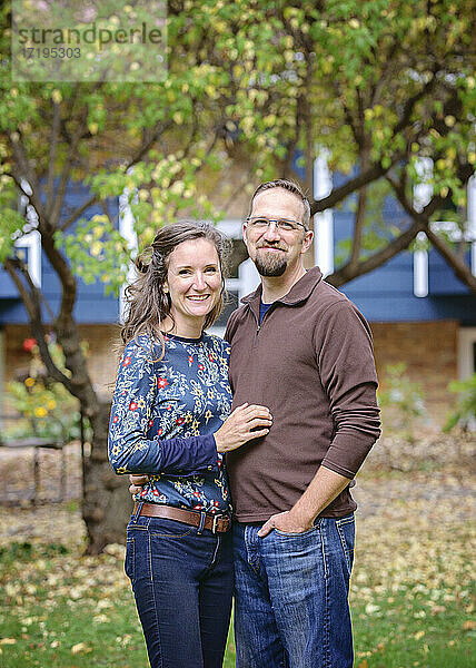 Glückliches Paar vor einem blauen Haus und Bäumen.