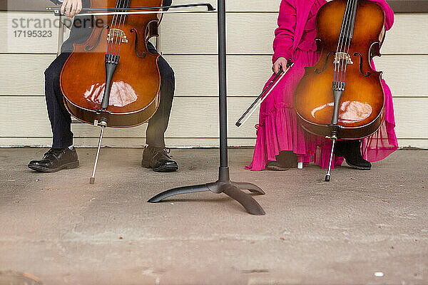 untere Hälfte von zwei Cello spielenden Kindern auf einer Veranda in ausgefallener Kleidung