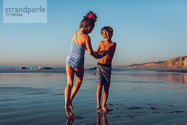 Junge und Mädchen spielen am Strand zur goldenen Stunde Ring um die Rose.