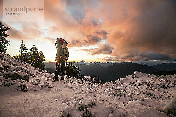 Abenteuerlustiger Rucksacktourist auf einem verschneiten Berggipfel.