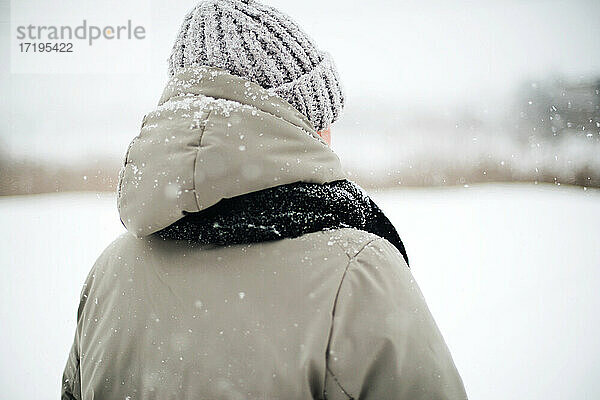 Frau steht auf verschneiter Straße und betrachtet eine Schneelandschaft