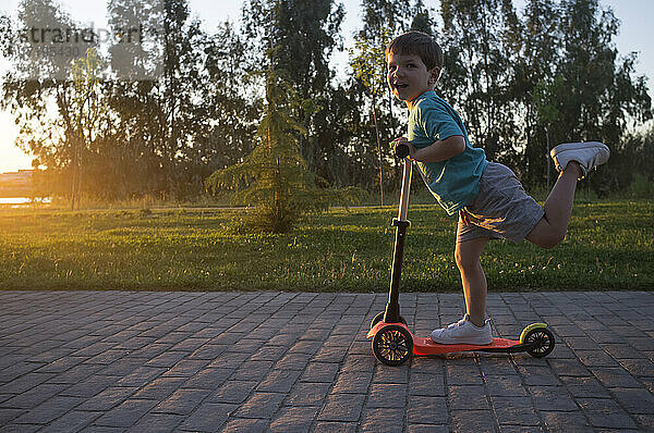 3 Jahre Junge fährt einen Roller einen schönen sonnigen Frühling Sonnenuntergang