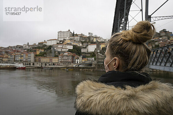Ein Tourist trägt eine Gesichtsmaske und bewundert die Brücke Dom Luis I und den Fluss Douro