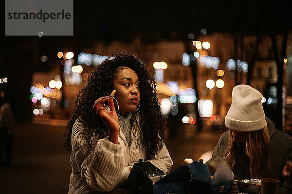 Junge Frauen essen Straßenessen am Tisch in der Stadt bei Nacht