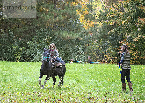 Frau mit einem Pony an der Leine  das ein junges blondes Mädchen trägt.