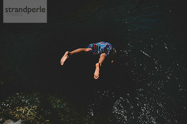 Fliegende Füße  als Junge im bunten Anzug ins dunkle Wasser taucht