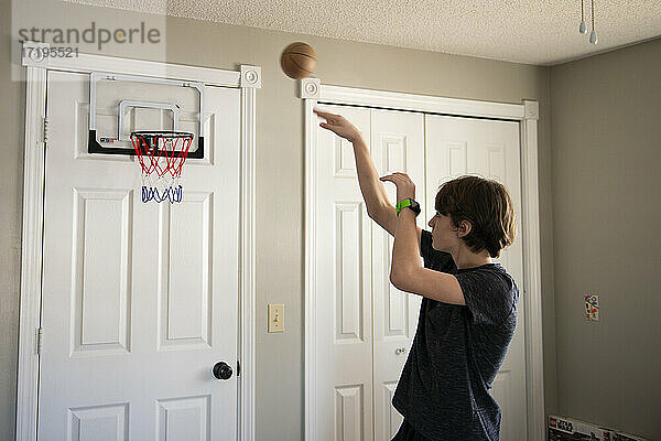 Ein kleiner Junge wirft einen kleinen Basketball in seinem Zimmer.