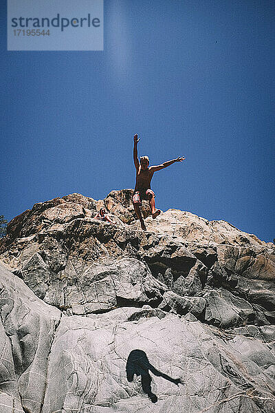 Teenager-Junge springt von Klippe mit blauem Himmel hinter sich