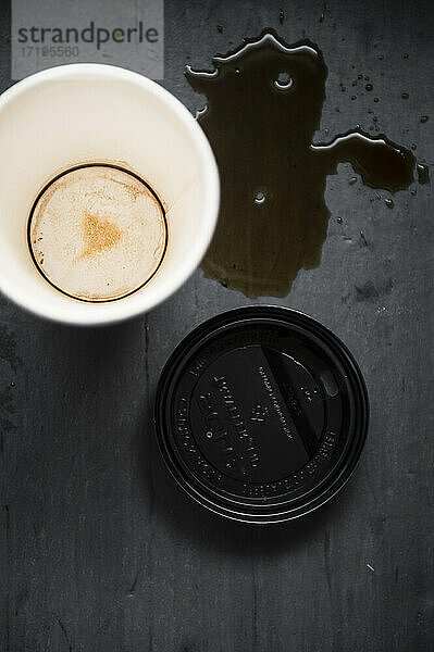 Verschütteten Kaffee mit leeren Papier Kaffeebecher und Deckel auf schwarzem Hintergrund
