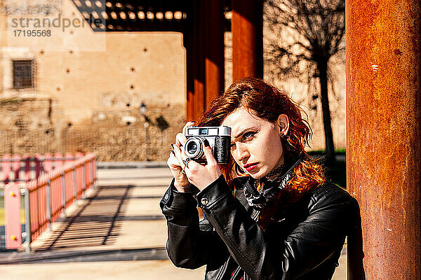 Alternatives Mädchen mit blauen Augen und orangefarbenen Haaren macht ein Foto mit ihrer Vintage-Kamera.