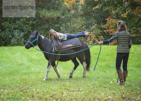 Frau mit Pony an der Leine  die ein junges blondes Mädchen balanciert.