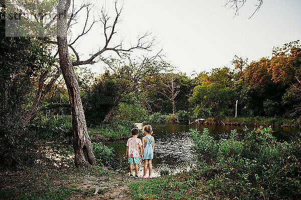 Junger Bruder und junge Schwester stehen am Ufer eines Sees und suchen nach Fischen