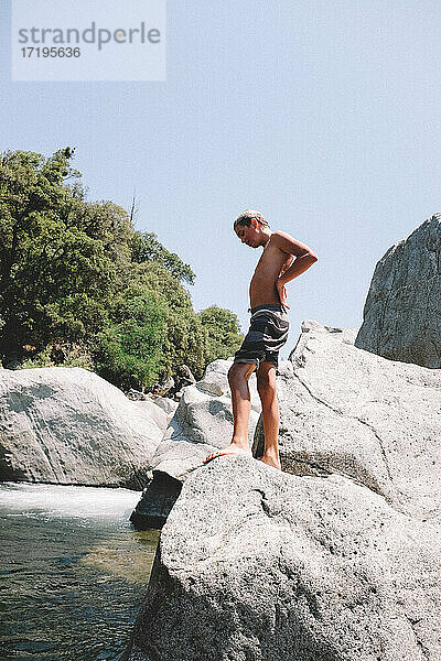 Kleiner Junge erwägt Sprung von einem Felsen am Fluss