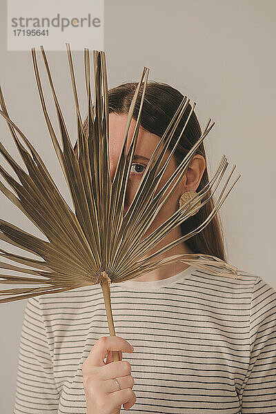 Porträt einer Frau  die durch ein Palmenblatt schaut. Junge Kaukasierin