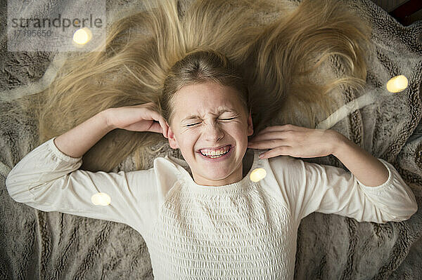 Junges Mädchen lachend auf Decke umgeben von Lichterketten