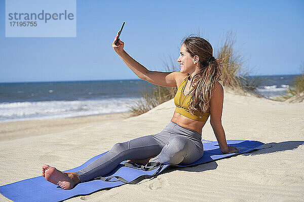 Mädchen  das ein Selfie macht  während es am Strand Yoga übt.