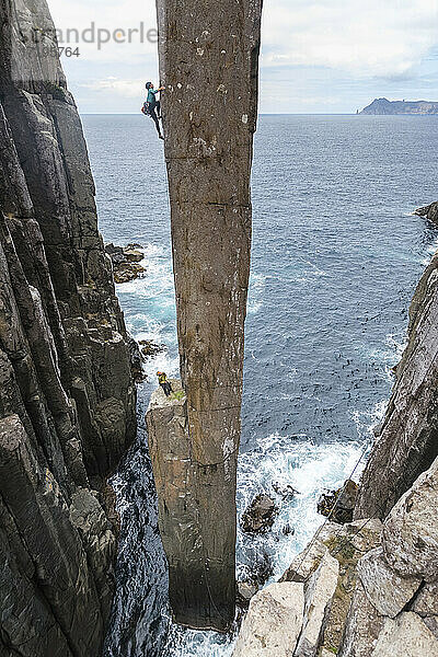 Eine Kletterin klettert auf den Totem Pole  eine Felssäule im Ozean.