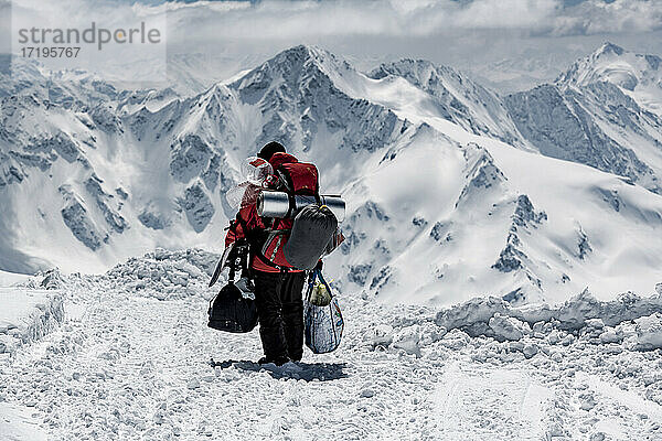 Rückansicht eines männlichen Wanderers  der Taschen trägt  während er auf einem verschneiten Berg im Urlaub wandert