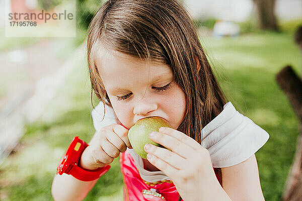 Ein junges Mädchen isst eine frisch gepflückte Birne in ihrem Hinterhof.