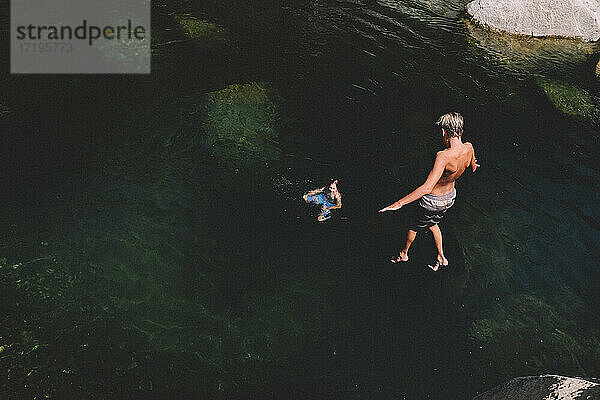 Junge schwebt mitten im Sprung  während sein Freund vom Wasser aus zuschaut