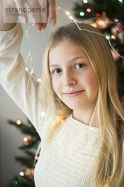 Porträt eines Mädchens zwischen zwei und drei Jahren  das Lichterketten am Weihnachtsbaum hält