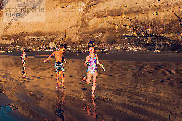 Drei kleine Kinder rennen bei Ebbe und Sonnenuntergang am Strand entlang.