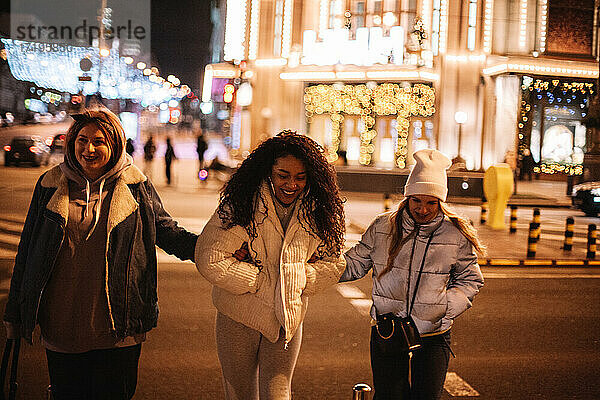 Glückliche Freundinnen beim Überqueren der Straße in der Stadt bei Nacht