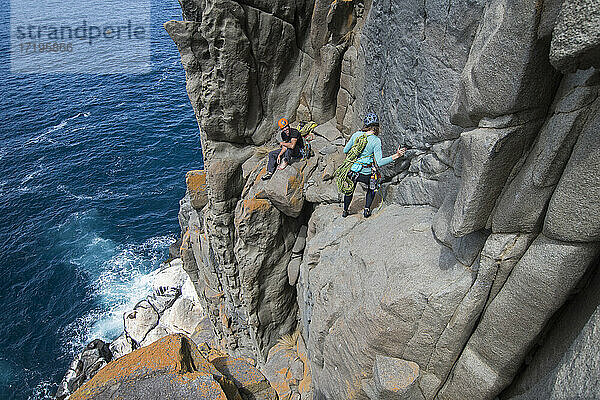 Ein Paar unerschrockener Bergsteiger erkundet die spektakulären Klippen von Cape Raoul in Tasmanien  Australien  und lächelt sich gegenseitig zu  während sie das exponierte Gelände oberhalb einer Robbenkolonie durchqueren.