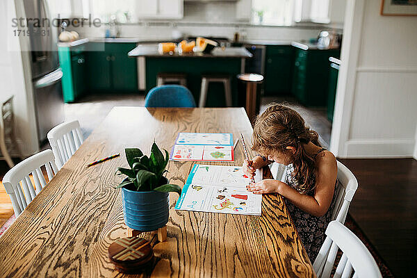 Junges Mädchen schreibt in Kindergarten Arbeitsbuch in modernen Haus