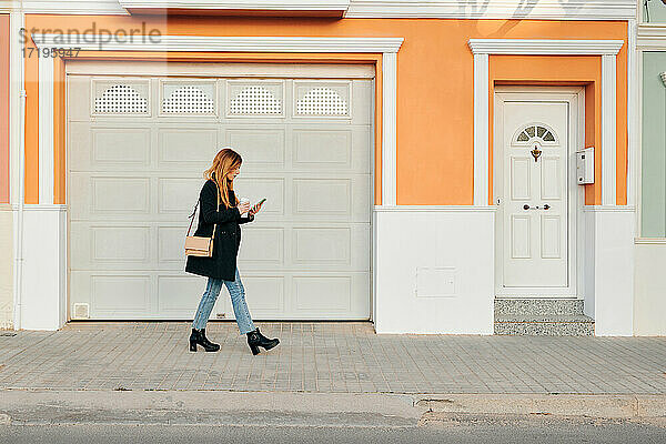 Frau geht auf der Straße  während sie auf ihr Smartphone schaut