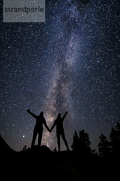 Silhouette Paar hält sich an den Händen  während gegen Sternfeld in der Nacht im Urlaub stehen