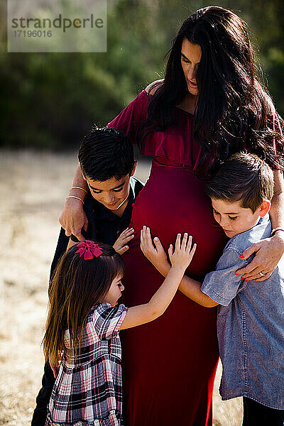 Kinder umarmen schwangere Mutter auf einem Feld in San Diego