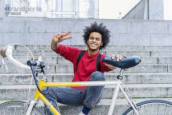 junger Mann mit Afro-Haar  der neben seinem alten Fahrrad sitzt