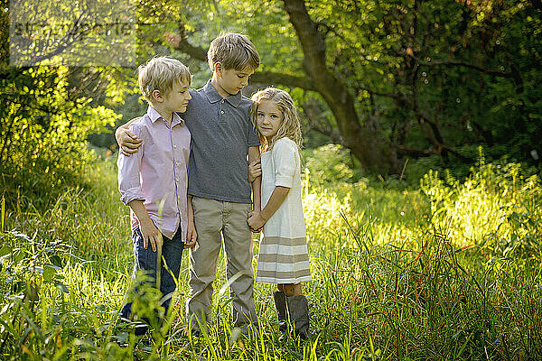 Drei liebevolle blonde Kinder stehen zusammen auf einer goldenen Wiese