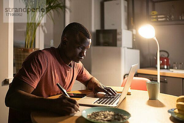Intelligenter schwarzer Mann  der einen Laptop benutzt und sich Notizen macht