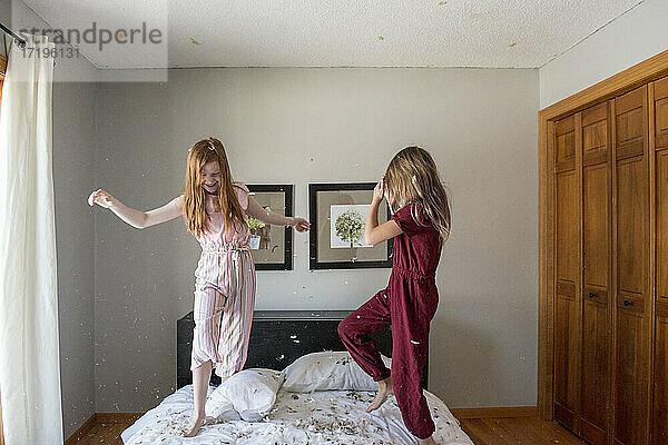 Zwei glückliche junge Mädchen  die auf dem Bett eine Federkissenschlacht machen.