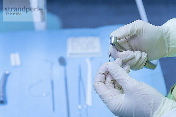 Zahnarzt mit Handschuhen an den Händen bei der Vorbereitung des Bohrers in einer Zahnklinik