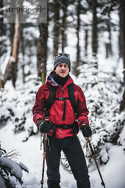 Porträt eines männlichen Skifahrers mit roter Jacke in einem verschneiten Wald in Maine
