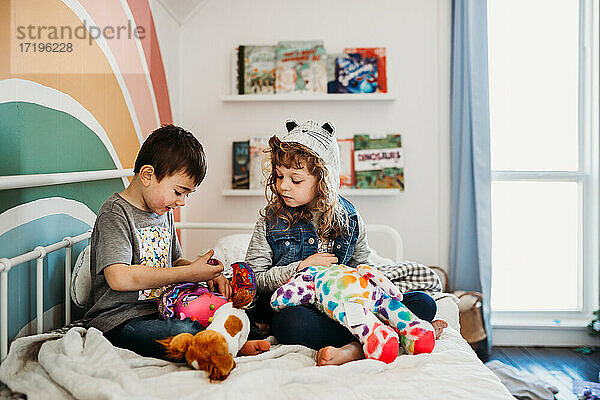 Bruder und Schwester sitzen auf dem Bett im Regenbogenkinderzimmer und spielen