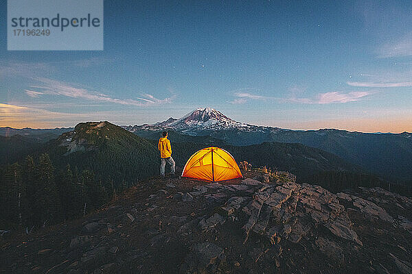 Ein Mann steht bei einem Zelt auf dem Gipfel eines Berges in der Nähe des Mount Rainier. Rainier