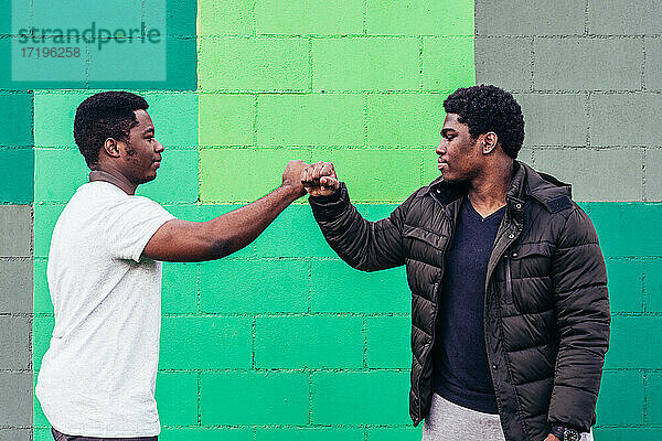 Porträt von zwei schwarzen Jungen  die sich auf einem grünen Wandhintergrund die Fäuste stoßen.