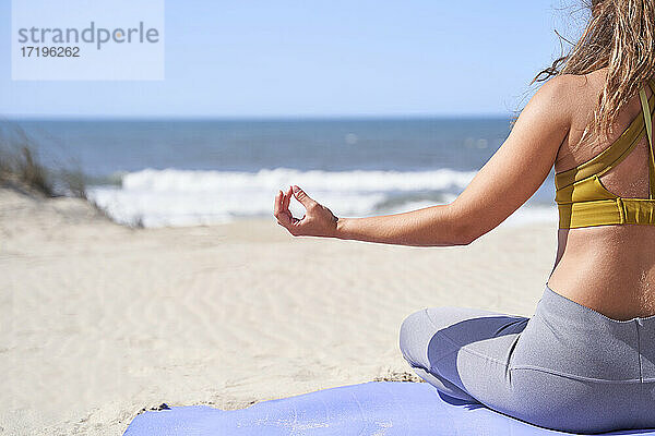 Nahaufnahme einer jungen Frau  die von hinten mit geschlossenen Fingern vor dem Meer eine meditative Geste macht.