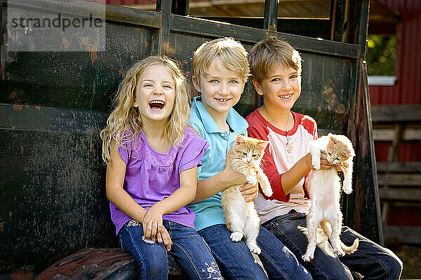 Drei glückliche blonde Kinder spielen mit Kätzchen im Freien.