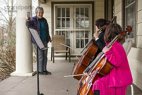 Eine ältere Frau nimmt zwei Kinder auf  die auf der Veranda ein Cellokonzert geben