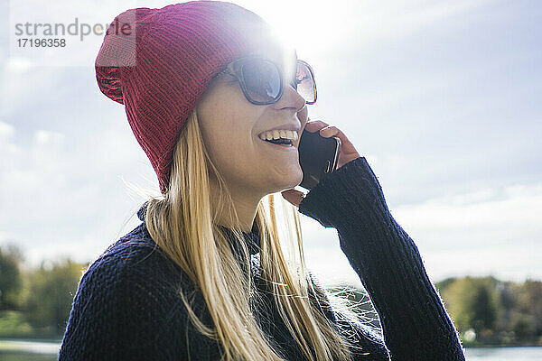 Junge blonde Frau im Park beim Telefonieren mit fröhlichen Ausdrücken
