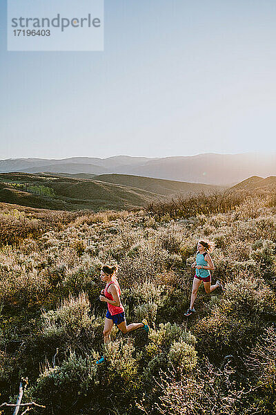 Zwei sportliche Frauen beim Trailrun in den Bergen zur goldenen Stunde